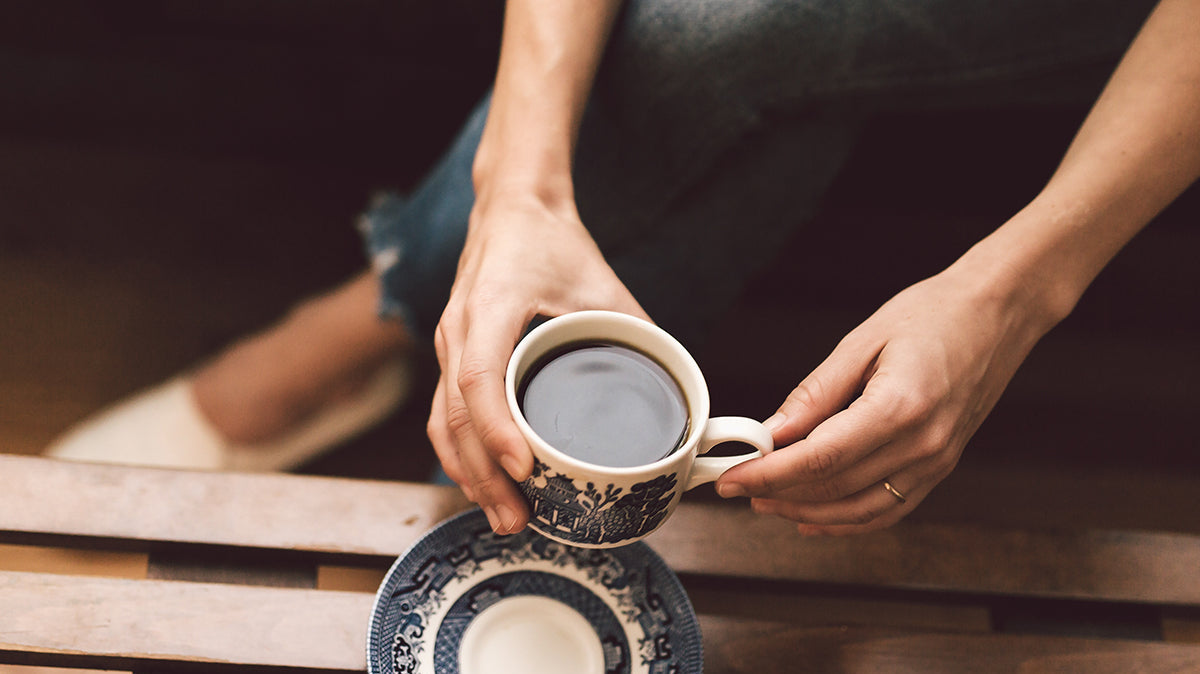 Person holding a cup of coffee over a table