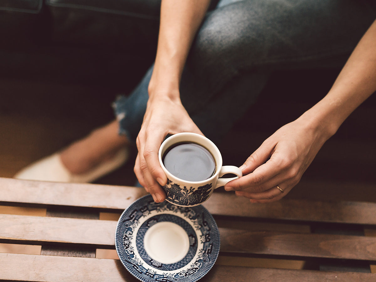 Person holding a cup of coffee over a table